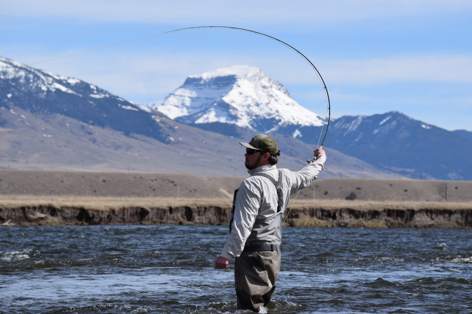 man wade fishing in river with mountain in background