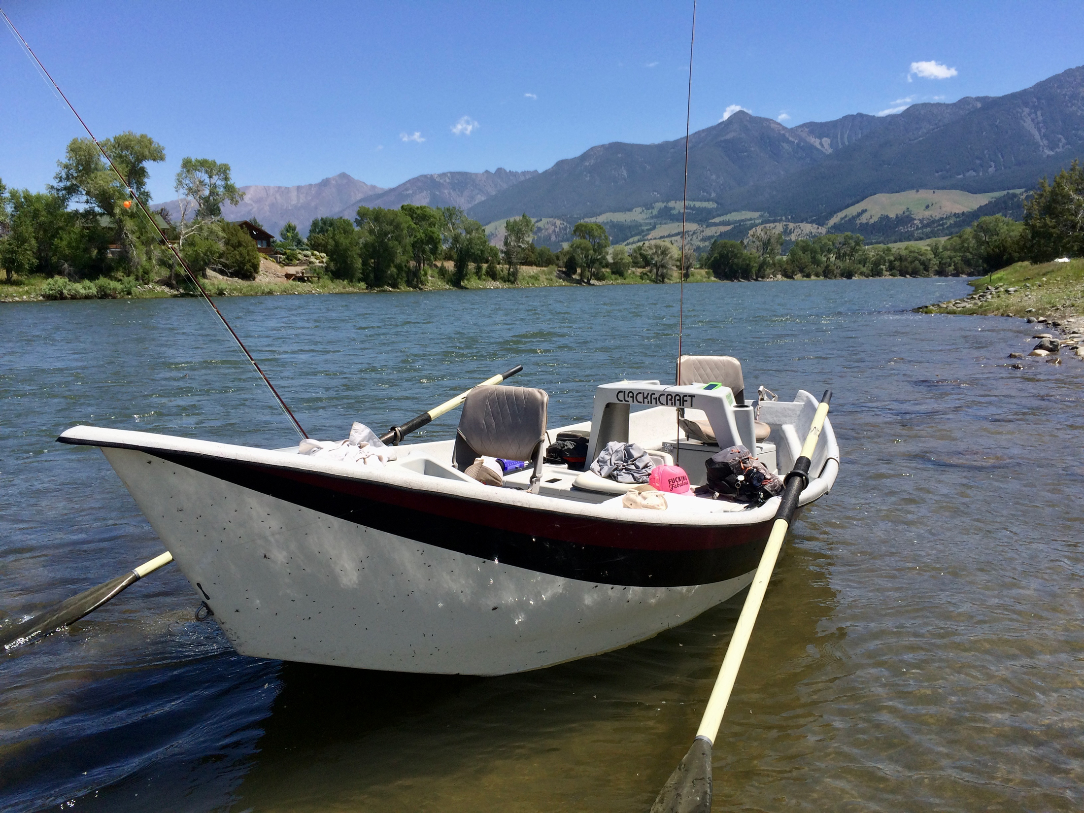 drift boat anchored in river with mountains in background
