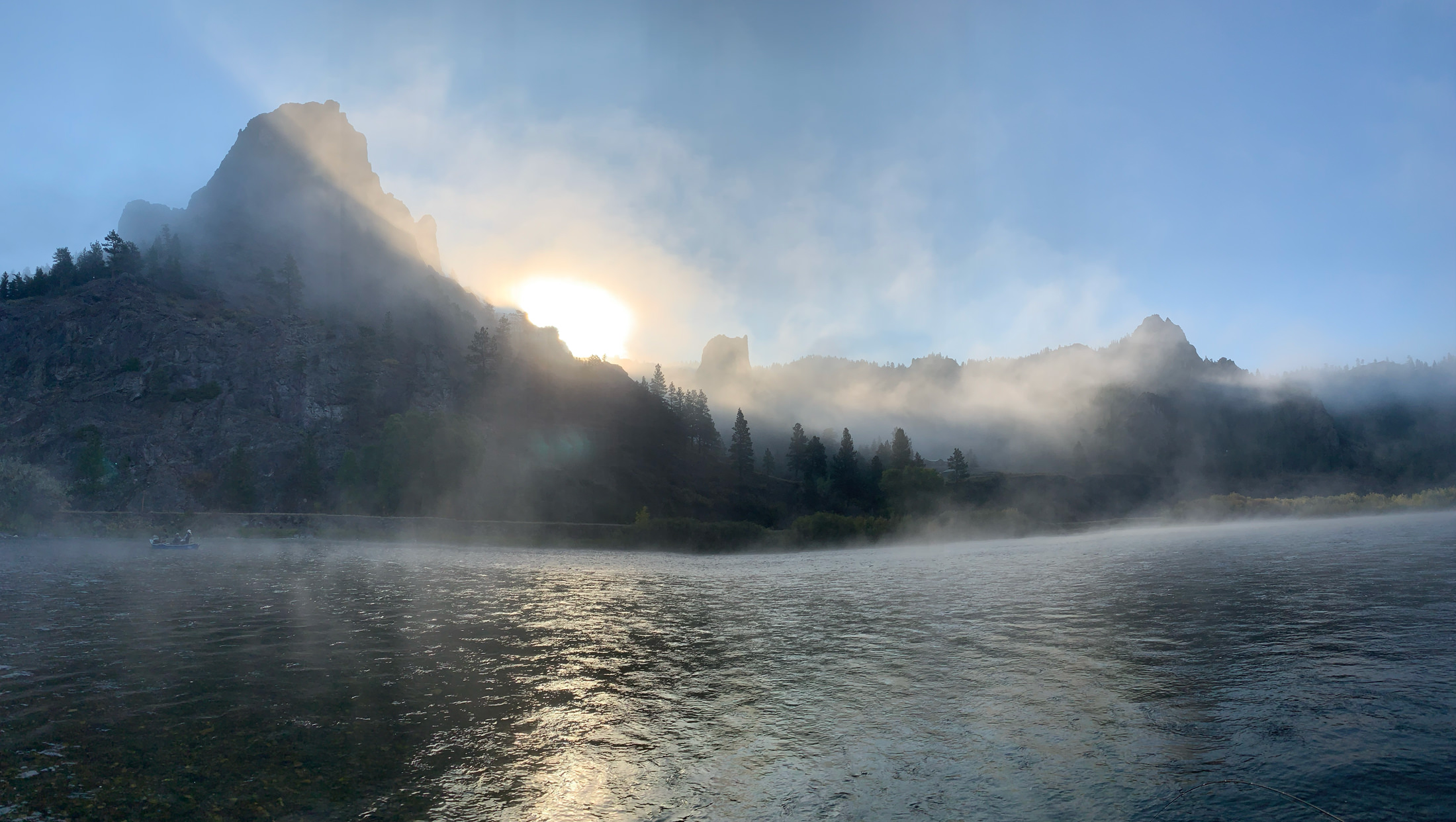 river in foreground with mountains and fog in background with rising sun